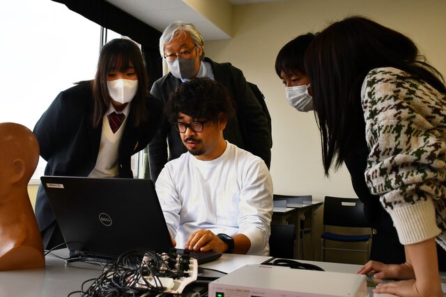 高校生や高校教員、大学生がモニターを覗き込んでいる写真
